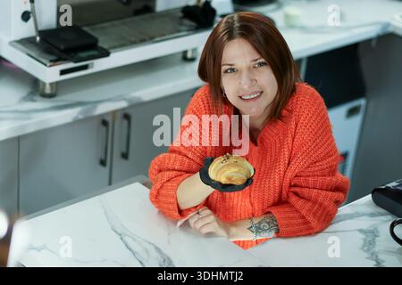 La donna casual in maglione presenta pasta sfoglia con guanto igienico all'interno Foto Stock
