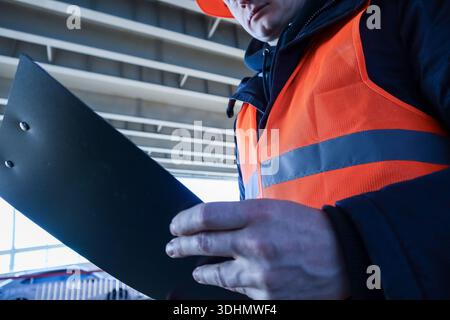 Primo piano estremo della mano maschile in un dispositivo di sicurezza che tiene il portadocumenti nero sotto la struttura del soffitto industriale. Foto Stock