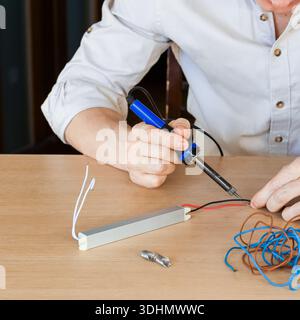 Primo piano della punta di saldatura che tocca la giunzione dei fili su una barra simile all'alluminio con utensili sparsi intorno Foto Stock