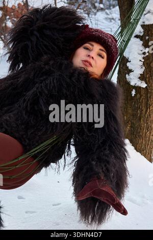 L'immagine cattura una donna in un momento di sereno relax in un ambiente invernale. È annidata in un'amaca, sospesa tra alberi innevati, cr Foto Stock