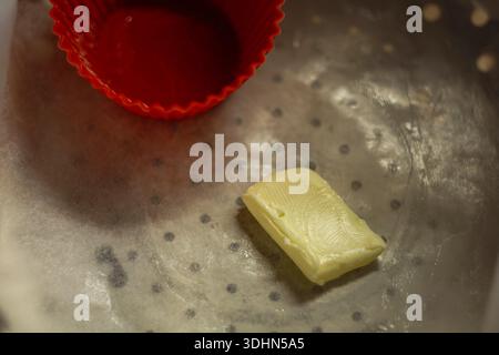 Un pezzo di burro che si scioglie in una padella calda. Inizio del processo di cottura con stampo in silicone rosso. Foto Stock
