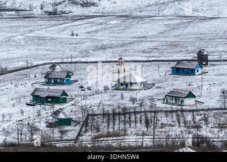 Un villaggio si trova sotto una coperta di neve. Le case colorate stanno al freddo. Al centro è visibile una piccola chiesa con un paesaggio tranquillo. Foto Stock
