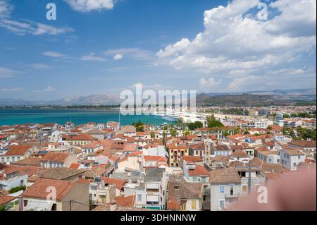 Nauplie, Grecia - 4 settembre 2024: Vista panoramica sopraelevata sulla città di Nauplie con tetti densamente pieni di tegole rosse, il porto con un grande yacht e montagne lontane sotto un cielo parzialmente nuvoloso. Foto Stock