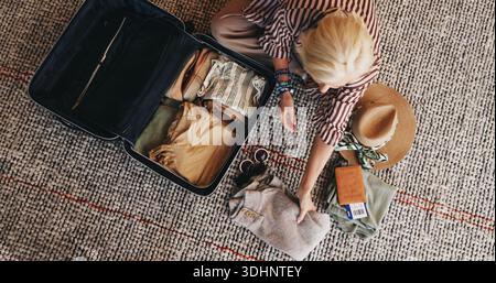 Donna, viaggia e porta con sé la valigia in casa per vacanze, vacanze o vacanze. Vista dall'alto, donna o viaggiatrice con abbigliamento, bagagli o. Foto Stock