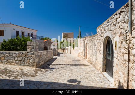 Aeropoli, Grecia - 11 settembre 2024: L'immagine mostra una stretta strada lastricata fiancheggiata da edifici tradizionali in pietra, muri in pietra e una casa residenziale bianca con persiane in legno sotto un cielo azzurro. Foto Stock