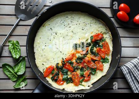 Una salata frittata o frittata con spinaci freschi e pomodori ciliegini in una padella. Sfondo in legno. Vista dall'alto. Foto Stock