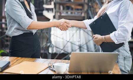 Due donne asiatiche architetto e ingegnere in caschi protettivi tremano la mano dopo l'incontro. Concetto di collaborazione di successo. Foto Stock