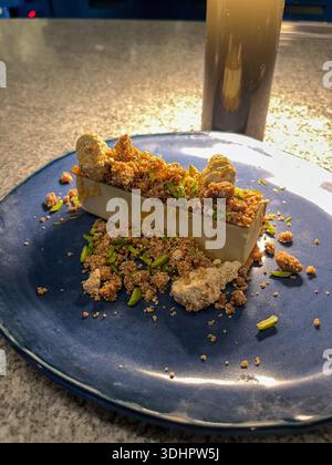 Un dessert bar rettangolare è splendidamente placcato su un piatto di ceramica blu, adornato con croccanti croccanti, pistacchi verdi e miele scintillante. Foto Stock