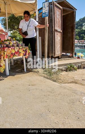 Corfù. Grecia - 22 gennaio 2026: Tradizionale bancarello del mercato greco con una donna locale che vende fichi e uva freschi in una soleggiata spiaggia mediterranea Foto Stock