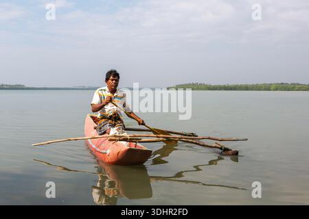 Pescatore seduto su un tradizionale e stretto peschereccio nella baia costiera dello Sri Lanka. Autentico stile di vita marittimo, tradizionale cultura della pesca e calma Foto Stock
