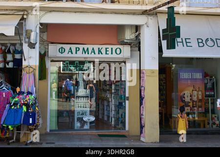 Corfù. Grecia - 22 gennaio 2026: Esterno commerciale di una tipica farmacia locale a Kerkyra con una classica croce verde al neon e una mediterranea Foto Stock