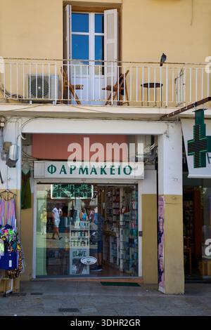 Corfù. Grecia - 22 gennaio 2026: Esterno di una tipica farmacia locale (Farmakeio) in Grecia con un cartello verde a croce e una residenza mediterranea Foto Stock