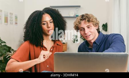 Due giovani professionisti collaborano su un notebook durante la riunione del team di avvio presso Modern Office Today Workspace Foto Stock