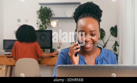 Happy Professional al telefono in un ufficio luminoso e moderno con un membro del team alla scrivania Foto Stock