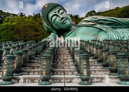 Vista di una colossale statua di Buddha sdraiata in bronzo riposa serenamente sopra gradini di pietra adornata con colonne ornate nel Tempio di Nanzoin, Sasaguri, Fukuoka Pr Foto Stock