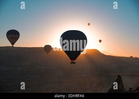 Cappadocia, Türkiye - 3 ottobre 2024: Palloni aerostatici fluttuano sul paesaggio roccioso della Cappadocia durante un tour in mongolfiera all'alba Foto Stock