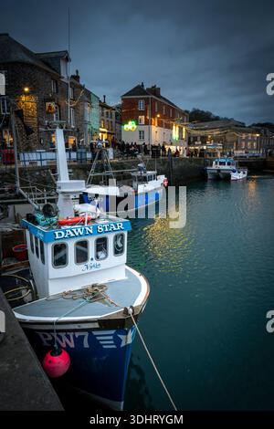 Barca da pesca *Dawn Star* (PW7) ormeggiata nel porto interno di Padstow di notte, con edifici storici sul porto illuminati dalle luci natalizie a Cornwa Foto Stock