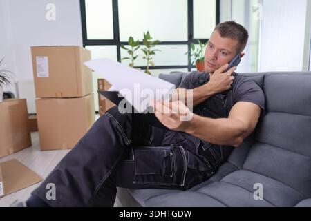 Il lavoratore impegnato esamina i documenti al telefono mentre è seduto in un ufficio moderno Foto Stock