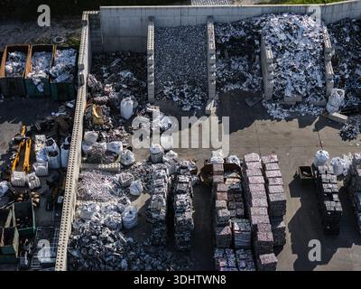 Grandi cumuli di rottami metallici e materiali lavorati sono visibili in un deposito di riciclaggio industriale con macchinari pesanti in funzione. Foto Stock