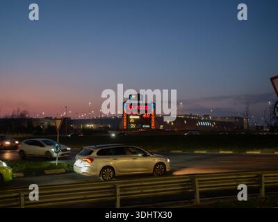 Cremona, Italia 8 gennaio 2026 Un grande complesso commerciale a Cremona, Italia, si illumina di insegne al neon quando i veicoli passano durante l'orario del crepuscolo Foto Stock