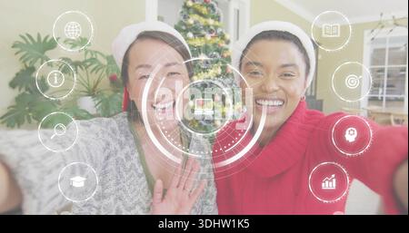 Sorridendo due donne che sbattono e si appoggiano insieme nel salotto di casa, indossando cappelli di Babbo Natale, rivestimento HUD Foto Stock