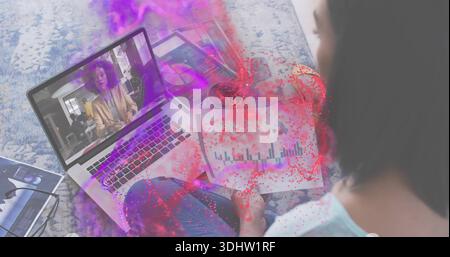 Donna che studia con la parte superiore azzurra che tiene le carte mentre guarda il laptop su un tappeto a motivi geometrici, la casa, lo spazio di copia Foto Stock