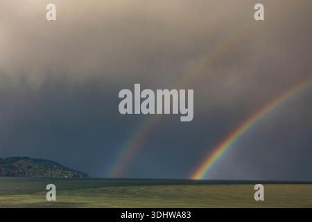 Un doppio arcobaleno in un cielo buio e tempestoso, che scende fino all'orizzonte. Foto Stock