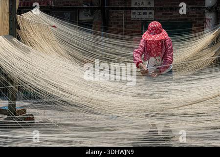 Veduta della cascata di spaghetti baciati dal sole intorno a un lavoratore in un cappello rosso floreale, creando un velo etereo all'aria aperta, Taichung, Taichung, Taiwan. Foto Stock