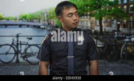 L'uomo si trova accanto al canale con un distintivo visibile sull'uniforme accanto alle biciclette parcheggiate vicino all'acqua in strada all'aperto; servizio. Foto Stock