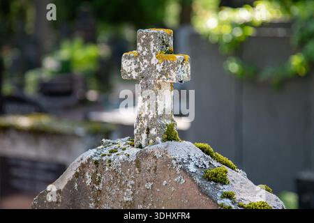 Primo piano di una piccola croce di pietra bianca, coperta di licheni, su un'antica lapide del cimitero Hietaniemi di Helsinki, Finlandia Foto Stock
