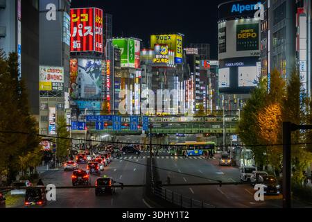 Una vista notturna di Shinjuku, Tokyo, che guarda su Ome-kaido Avenue mentre un treno della linea Yamanote arriva alla stazione di Shinjuku Foto Stock