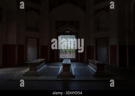 Delhi, India - 30 marzo 2024: L'immagine mostra tre tombe di marmo all'interno di una camera poco illuminata presso la tomba di Humayun, con una finestra a reticolo decorativa sullo sfondo. Foto Stock