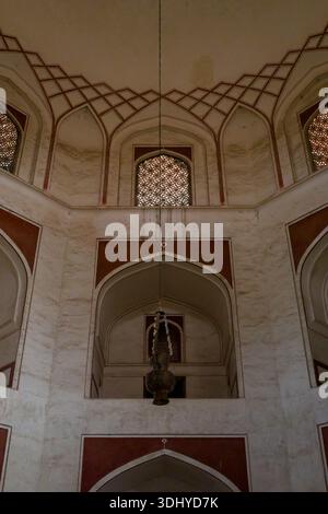Delhi, India - 30 marzo 2024: L'immagine mostra le pareti interne superiori della tomba di Humayun con alcole ad arco, finestre a reticolo in jali decorativi e una grande lampada sospesa dal soffitto. Foto Stock