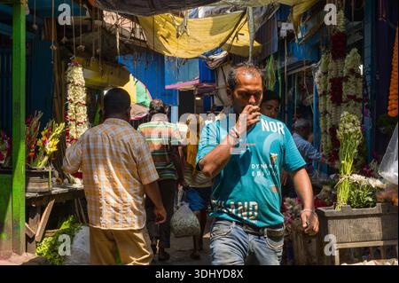 Calcutta, India - 24 marzo 2024: Le persone si vedono camminare e fare shopping tra bancarelle di fiori con ghirlande e fiori sfusi esposti in una stretta sezione coperta del mercato all'aperto di Calcutta. Foto Stock