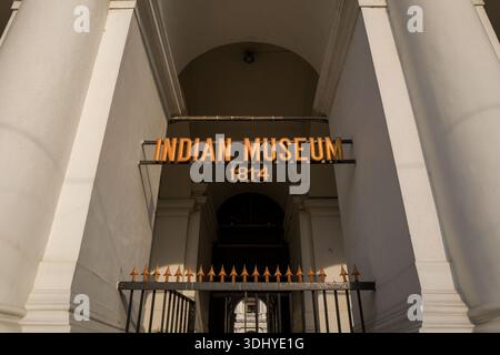 Calcutta, India - 24 marzo 2024: L'ingresso del Museo Indiano è esposto con un cancello metallico e un cartello arancione con la scritta "INDIAN MUSEUM 1814" montato sopra, incorniciato da colonne neoclassiche bianche e un passaggio ad arco. Foto Stock