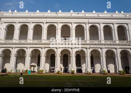 Calcutta, India - 24 marzo 2024: La facciata bianca neoclassica del Museo indiano è esposta con finestre ad arco, colonne e un prato in primo piano, con diverse persone e piante in vaso visibili al piano terra. Foto Stock