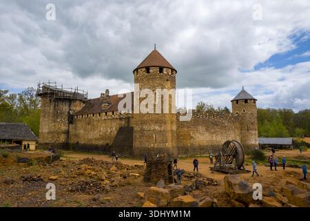 Castello di Guedelon, Francia - 20 aprile 2024: L'immagine mostra l'esterno del castello di Guedelon, un castello in stile medievale in costruzione con mura di pietra, torri rotonde, impalcature e una grande gru a ruote, con diverse persone che camminano intorno al sito. Foto Stock