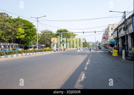 Calcutta, India - 24 marzo 2024: L'immagine mostra un'ampia strada nell'area dell'Esplanade con semafori in alto, un autobus pubblico blu, pedoni, negozi lungo la strada e alberi che fiancheggiano la strada sotto la luce del sole. Foto Stock
