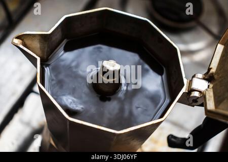 Primo piano di caffè fresco e scuro che viene erogato e che bolle nella camera superiore di una classica moka italiana, con il coperchio aperto, per catturare l'ultimo momento Foto Stock