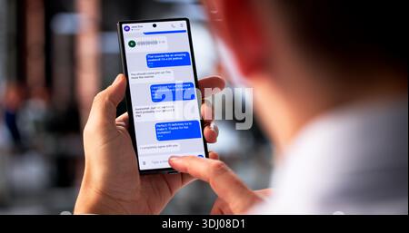 Uomo ispanico moderno che invia e-mail sul suo smartphone Inside Office Foto Stock