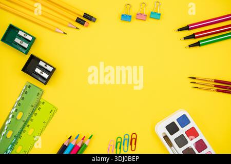 Piatto di coloratissime forniture scolastiche e artistiche su sfondo giallo con spazio per le copie. Foto Stock
