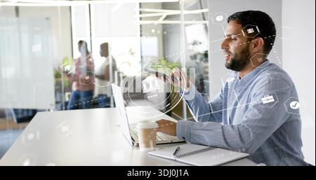 Lavoratore in camicia business-casual con smartphone e laptop in ufficio con HUD, spazio di copia Foto Stock