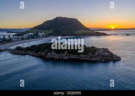 Vista aerea della luce dorata del sole che baciano le tranquille acque blu che circondano l'iconico Monte Maunganui, la regione Bay of Plenty, nuova Zelanda. Foto Stock