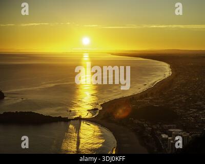 La vista aerea della luce dorata del sole si riflette sulle calme acque oceaniche lungo la costa vicino al Monte Maunganui, alla regione Bay of Plenty, nuova Zelanda. Foto Stock