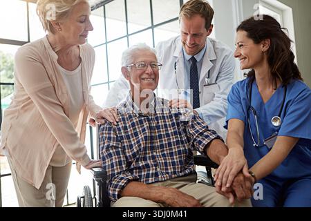Felice, medico e infermiere con senior man in clinica infermieristica per discussione di salute insieme. Coppia, check-up e paziente anziano di sesso maschile in sedia a rotelle Foto Stock