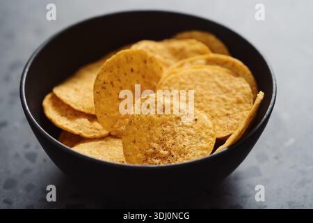 Nachos rotondi in una ciotola in ceramica nera su fondo in cemento Foto Stock