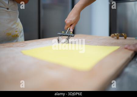 Chef professionista che prepara la tradizionale pasta fresca italiana con tortelli, tagliando la pasta con una taglierina per pasticceria in una cucina professionale, Foto Stock