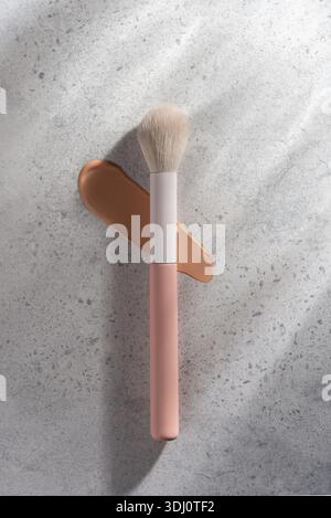 Spazzola per il trucco con spalmatura beige su fondo in cemento. Concetto di strumento cosmetico professionale che mostra la texture, la fusione e la routine di bellezza per S. Foto Stock