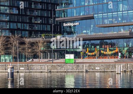 Moderna architettura in vetro della sede centrale del Booking.com a Oosterdokseiland ad Amsterdam, che si riflette sulla superficie dell'acqua. Foto Stock