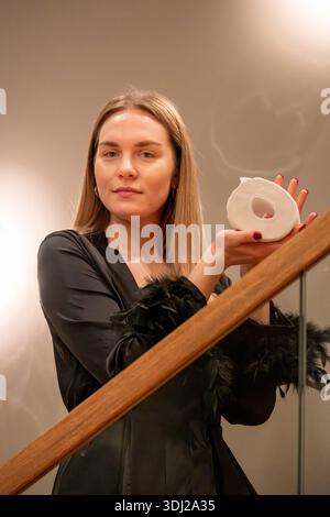 Una giovane donna con un abito nero si erge su una scala, reggendo un oggetto decorativo mentre l'illuminazione soffusa migliora il Foto Stock